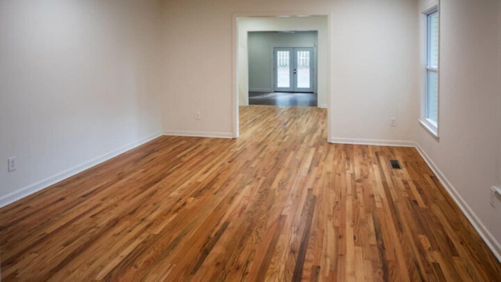 An empty living room with hardwood floors and bare walls, cleared and ready for a painting crew.