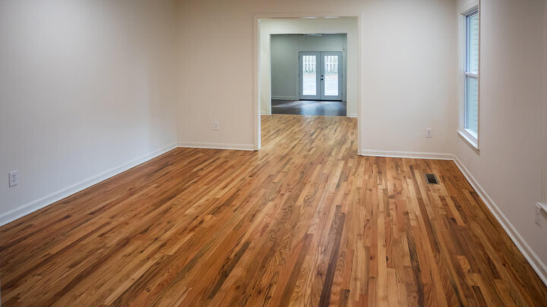 An empty living room with hardwood floors and bare walls, cleared and ready for a painting crew.