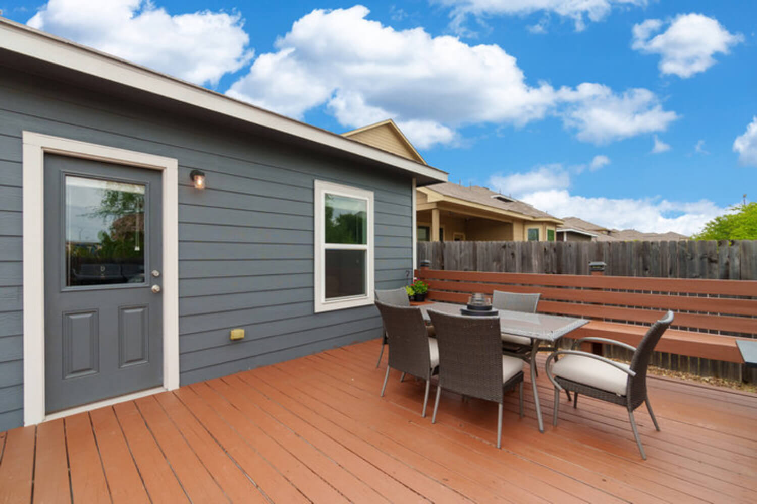 A backyard wood deck with a dining set, painted in a solid finish, next to a home with a wood privacy fence.